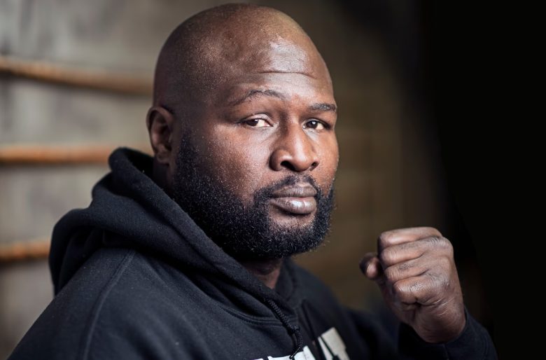 James Toney in a black hoodie, raising his fist in a boxing stance.