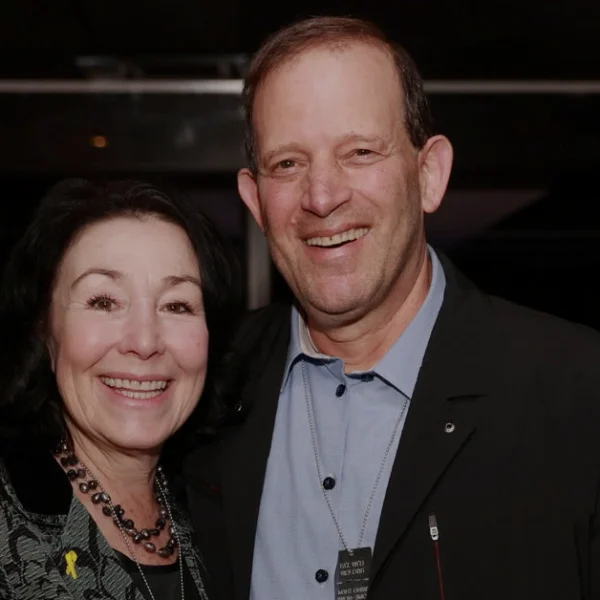 Gal Tirosh smiling with a woman at a formal event, both dressed elegantly and posing together in a warmly lit indoor setting.