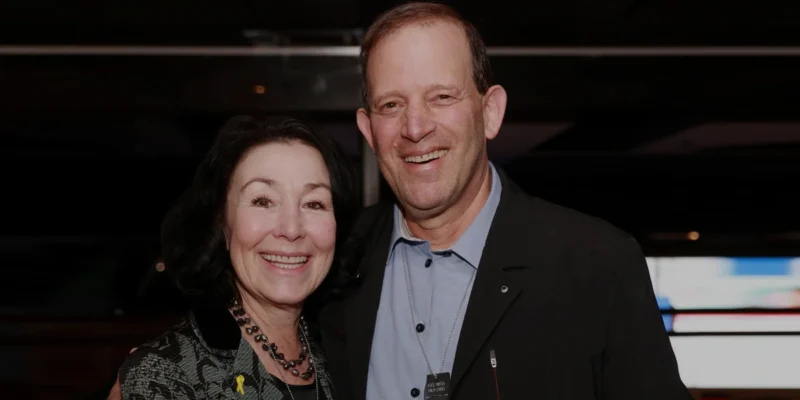 Gal Tirosh smiling with a woman at a formal event, both dressed elegantly and posing together in a warmly lit indoor setting.