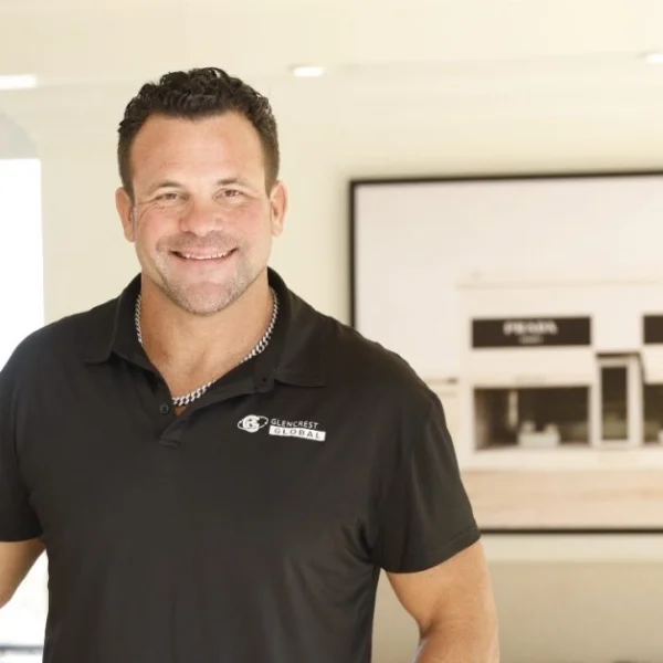 John Cerasani smiling in black Glencrest Global polo shirt in office doorway