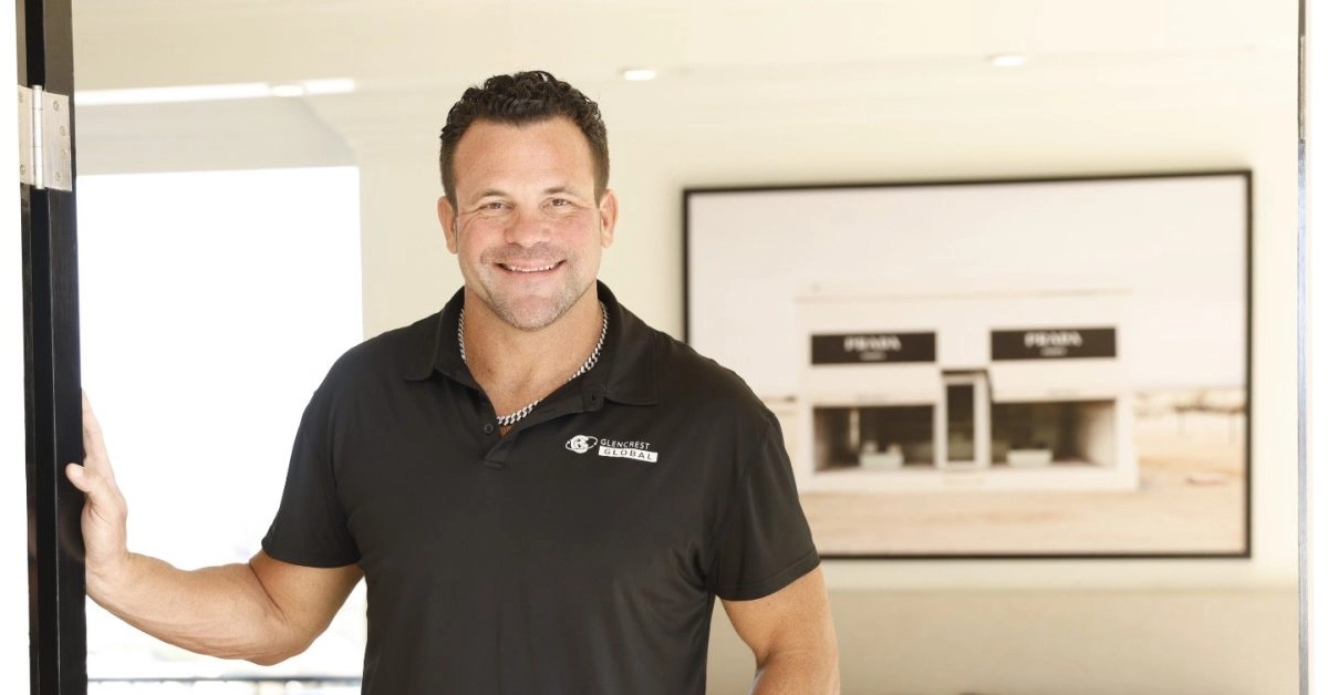 John Cerasani smiling in black Glencrest Global polo shirt in office doorway
