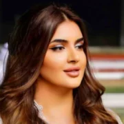 Princess Kazer at royal event wearing elegant white outfit with diamond necklace and styled brown hair