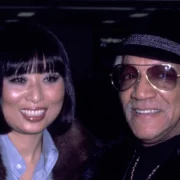 Kaho Cho smiling alongside comedy legend Redd Foxx at their wedding celebration in formal attire.
