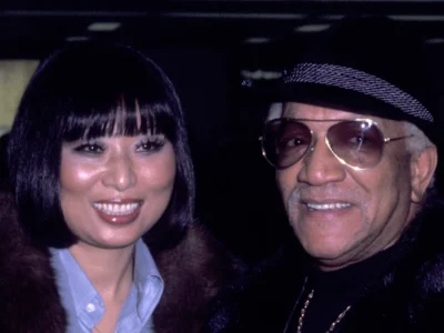 Kaho Cho smiling alongside comedy legend Redd Foxx at their wedding celebration in formal attire.
