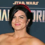 Gina Carano at The Mandalorian premiere, wearing a strapless dress and red headband, standing in front of the Star Wars backdrop.