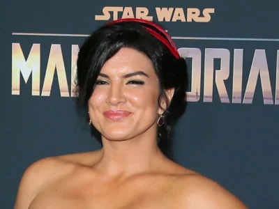 Gina Carano at The Mandalorian premiere, wearing a strapless dress and red headband, standing in front of the Star Wars backdrop.