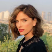 Noa Tishby Net Worth: Noa Tishby smiling confidently in a cityscape, representing her success as an actress, producer, and author.