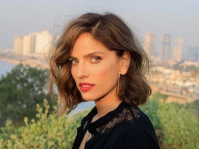 Noa Tishby Net Worth: Noa Tishby smiling confidently in a cityscape, representing her success as an actress, producer, and author.