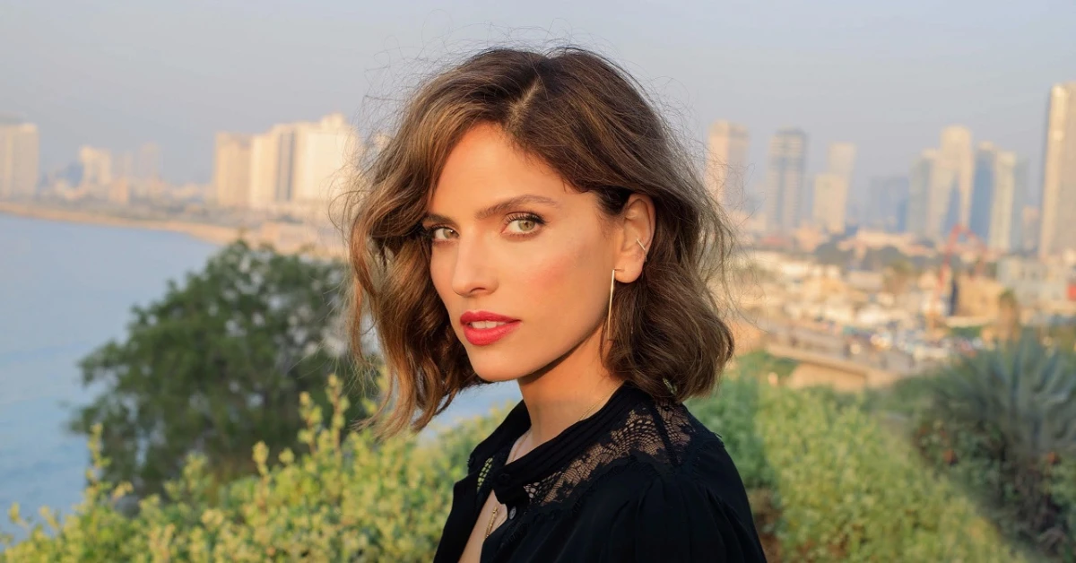 Noa Tishby Net Worth: Noa Tishby smiling confidently in a cityscape, representing her success as an actress, producer, and author.
